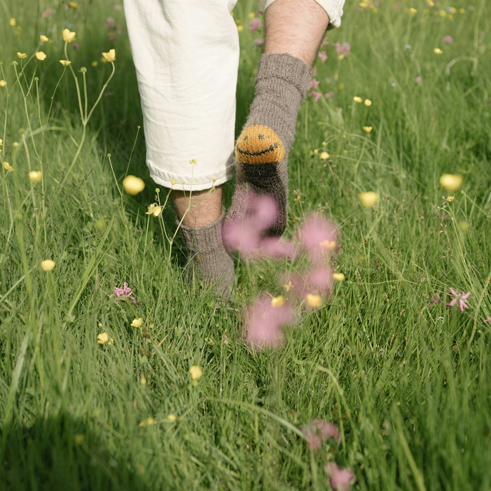 Person joyfully running with smiley socks in grass, surrounded by calming scent.